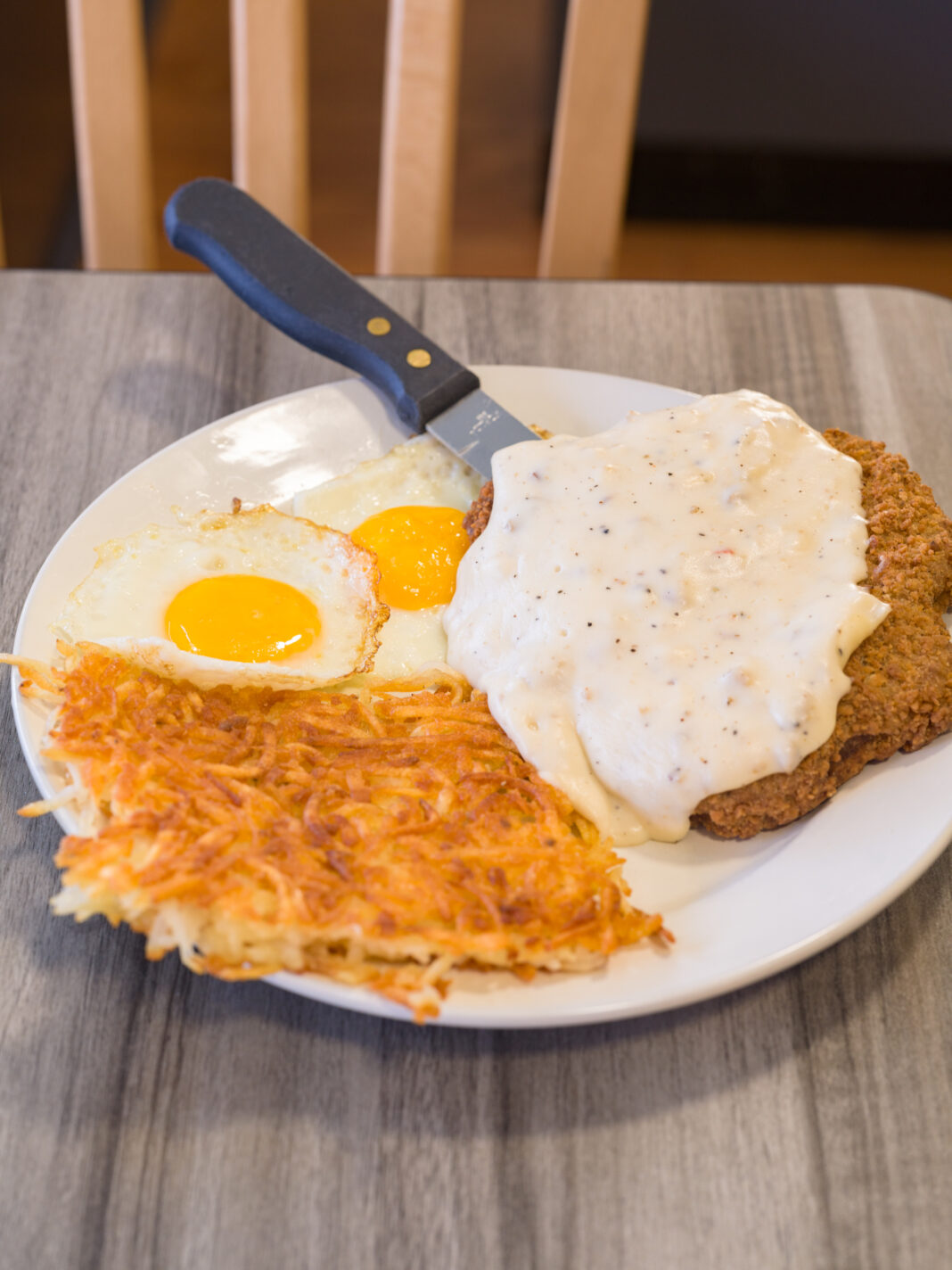 Chicken fried steak smothered in country gravy with two sunny-side-up eggs and hashbrowns